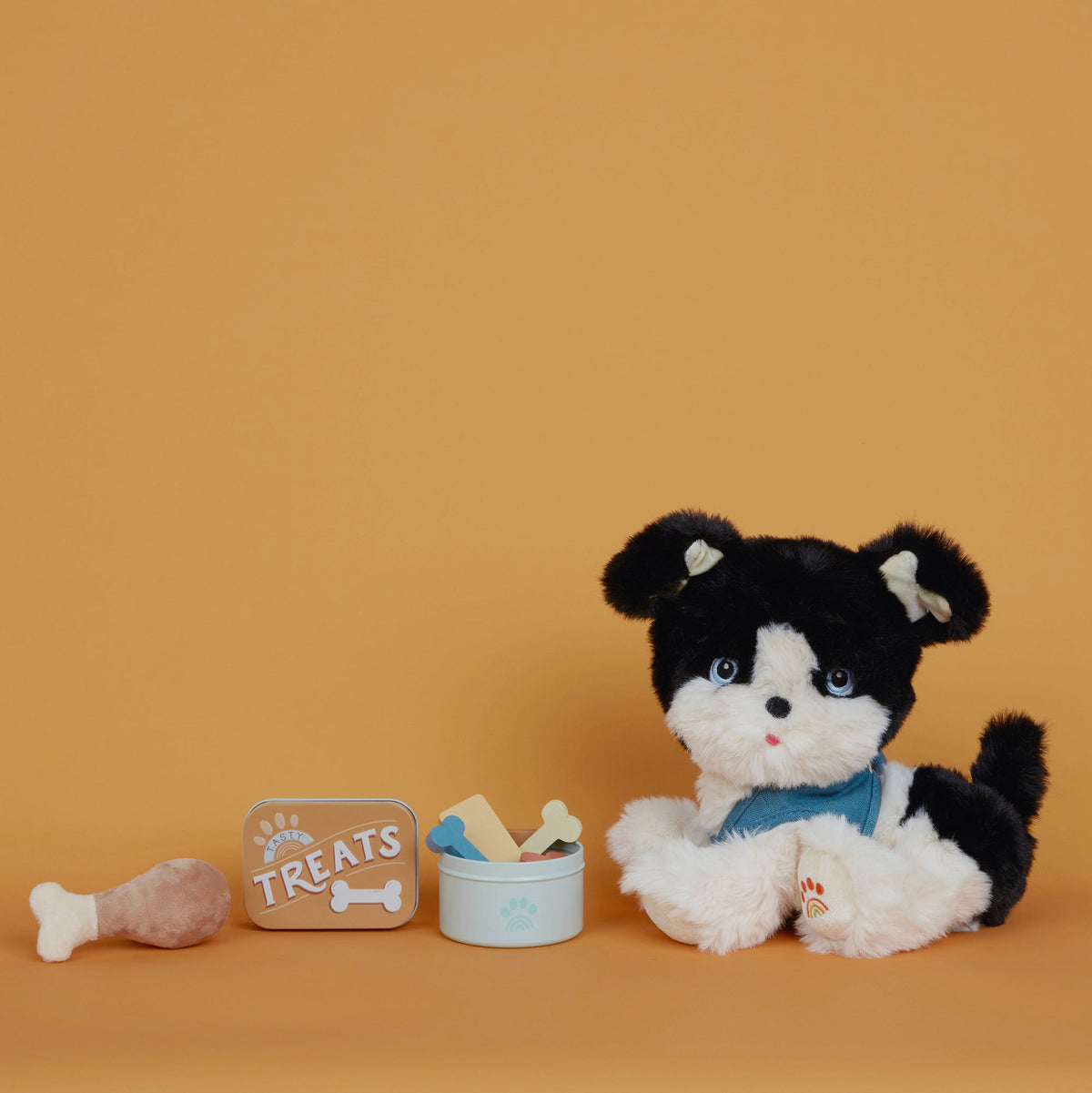 Black and white stuffed dog toy with a small container of treats on an orange background