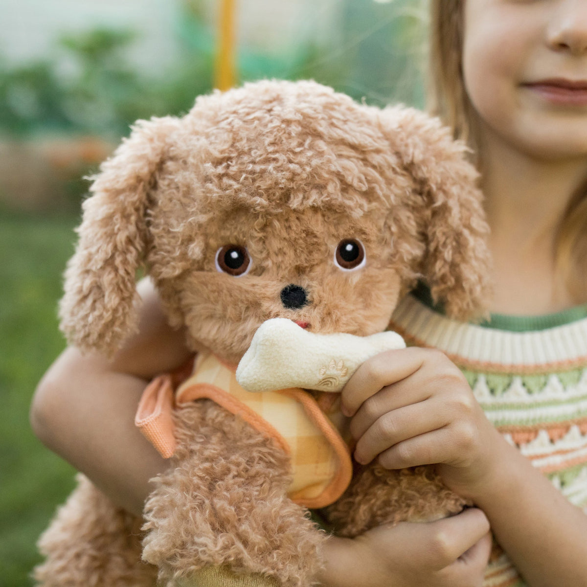 Child holding a brown teddy bear with a bone in its mouth outdoors