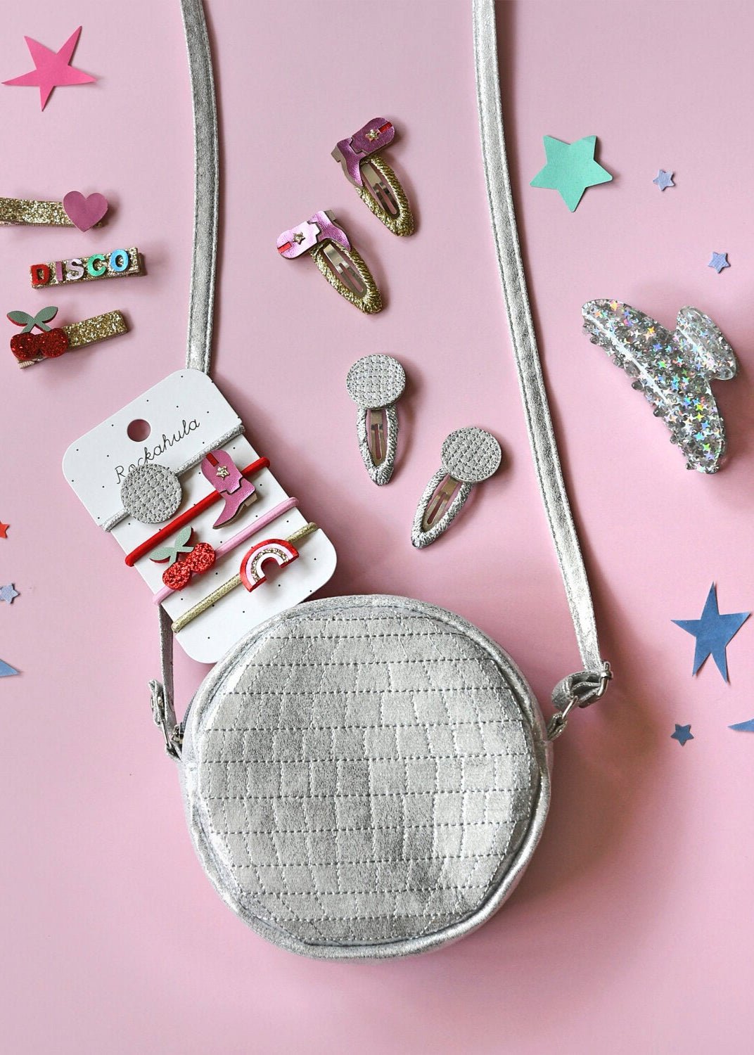 Small round silver bag with hair clips on a pink background