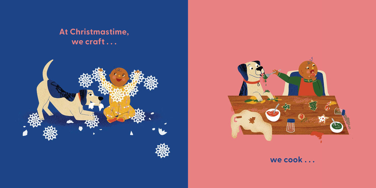 An interior spread from Dog's First Christmas featuring a split background of deep blue on the left and coral pink on the right. On the blue page, text at the top reads "At Christmastime, we craft..." while a white dog and a smaller dog stand amidst swirling paper snowflakes and a gingerbread figure. On the pink page, a table is piled with craft supplies, holiday cookies, and decorations, accompanied by text at the bottom that reads "...we cook...