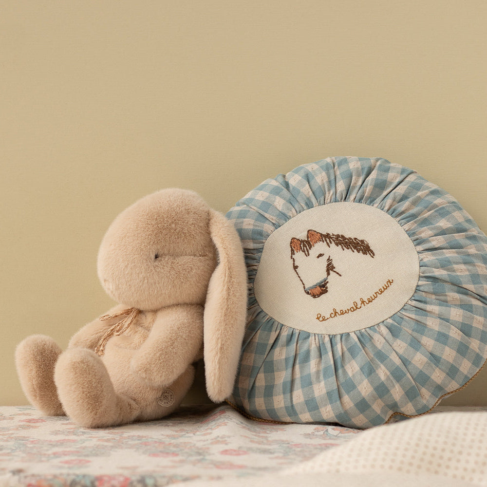 Plush toy and checkered pillow with embroidered design on a soft surface.