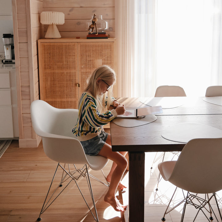 Woman sitting at a table in a bright room with large windows, reading a book.