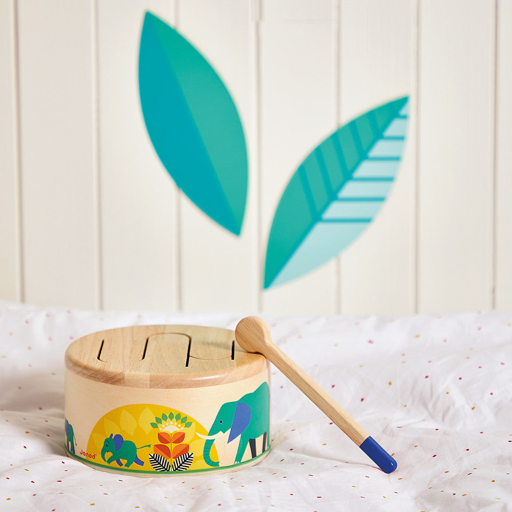 Children's wooden drum with elephant design and drumstick on a white surface with leaf decorations.