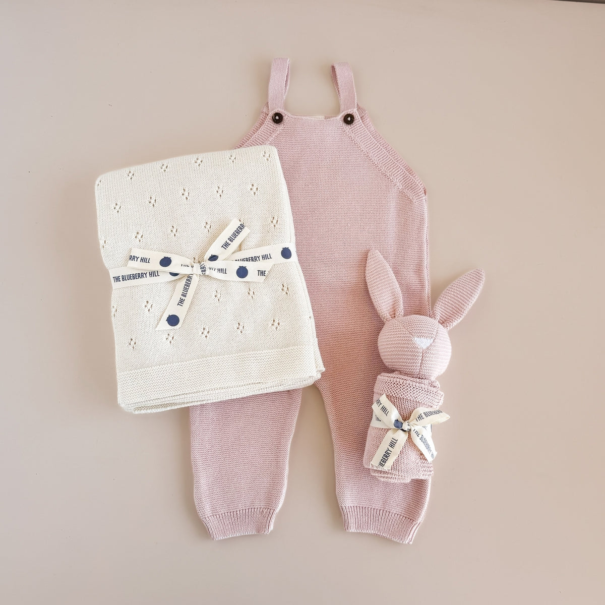 Baby outfit set with pink romper, matching pants, and bunny hat on a beige background