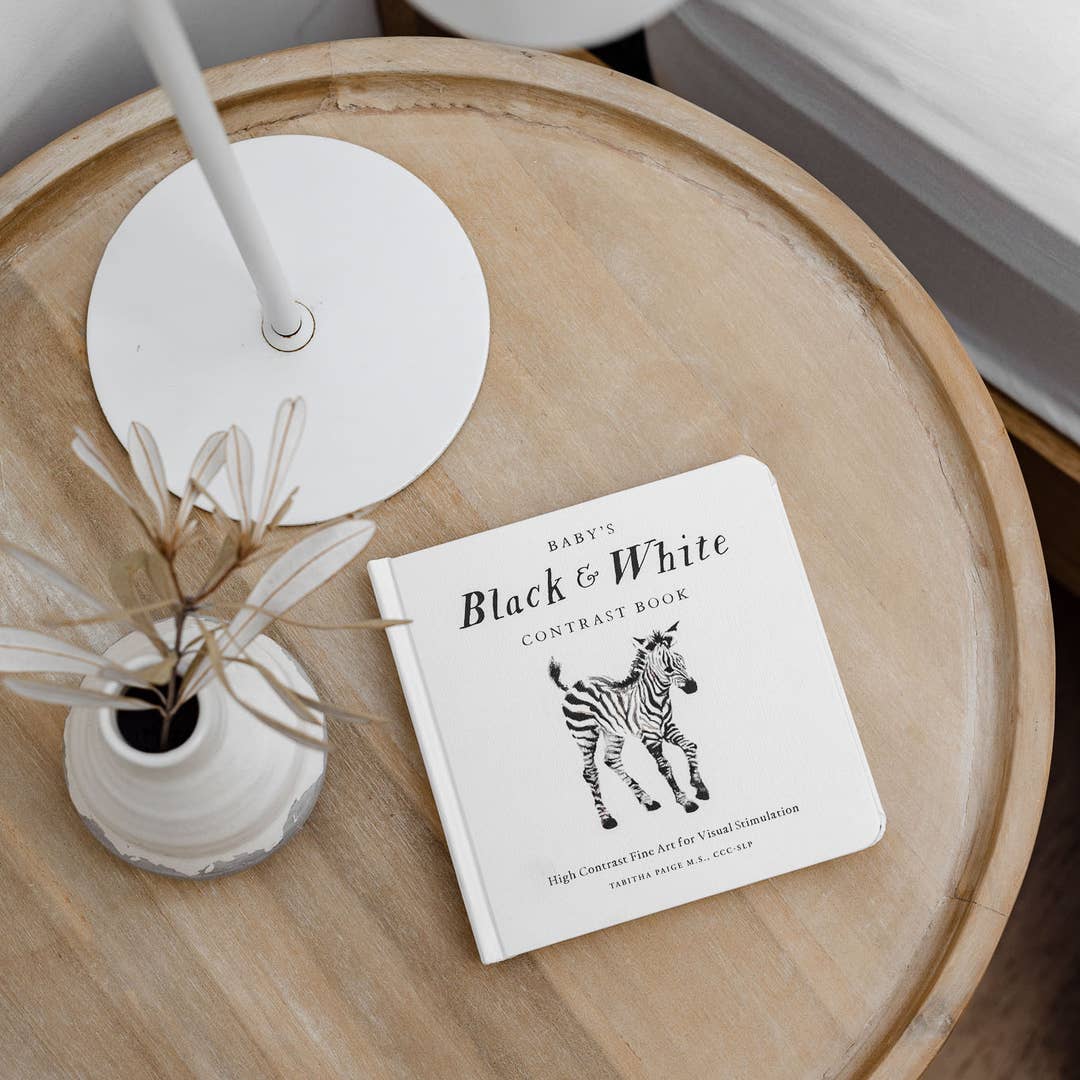 Children's book titled 'Black & White Contrast Book' on a wooden table with a vase and plant.