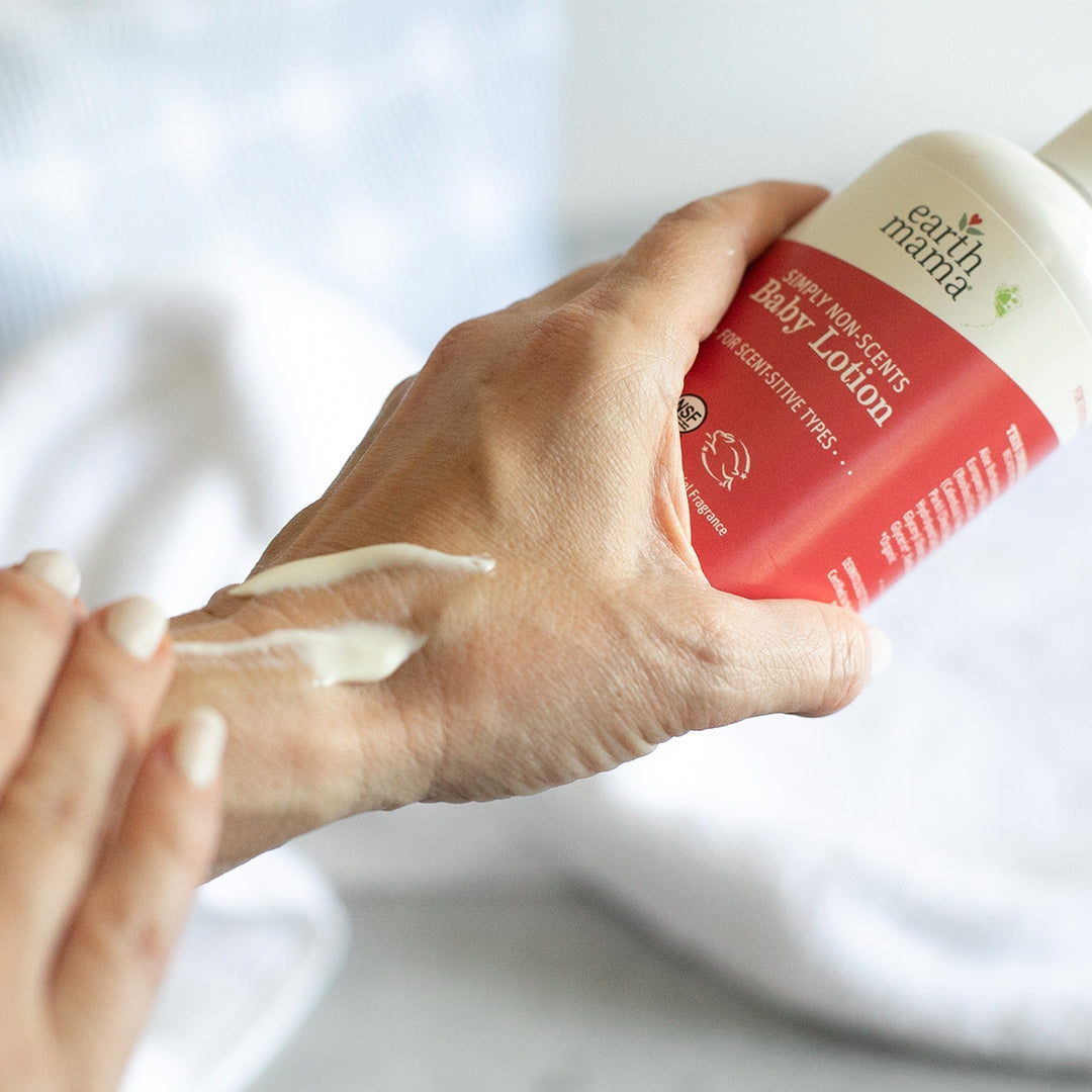 Hand applying lotion from a 'Earth Mama' bottle on a white background