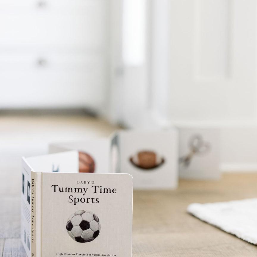 Children's book titled 'Tummy Time Sports' on a wooden surface with a blurred background