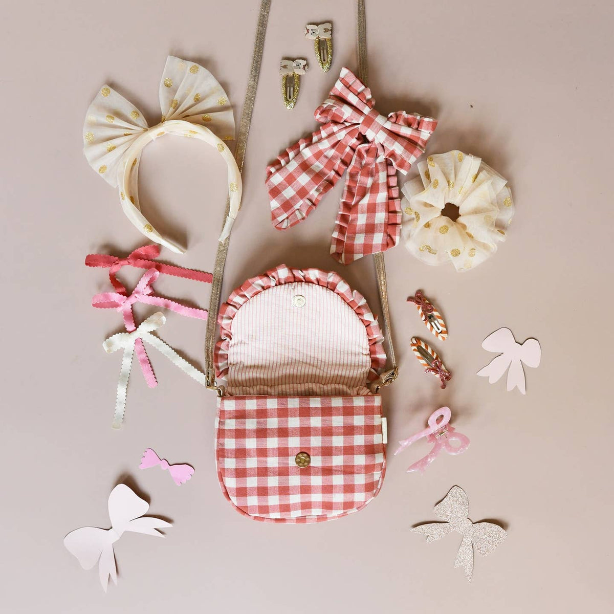 Collection of hair accessories including a red and white checkered bag, headbands, and ribbons on a beige background.