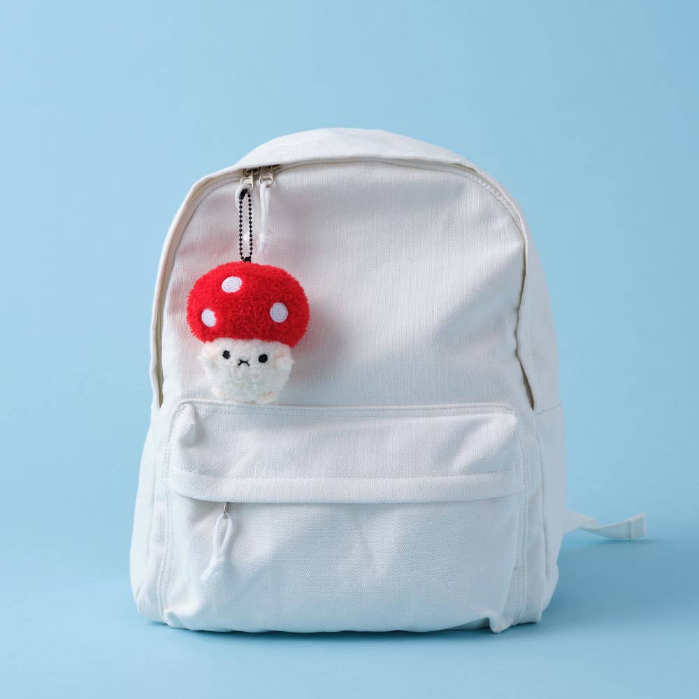 White backpack with a red and white mushroom-shaped keychain on a light blue background
