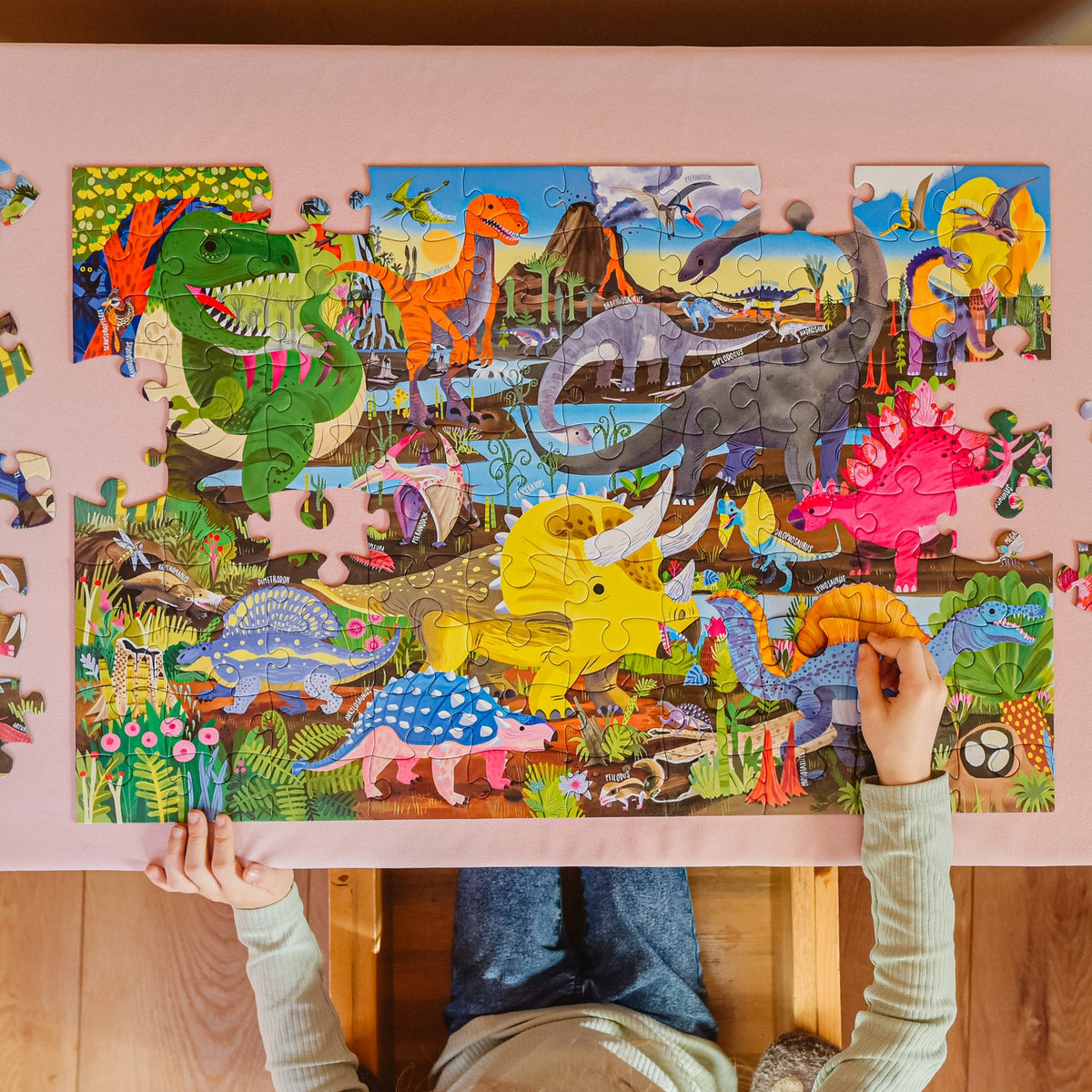 Child playing with a dinosaur puzzle on a pink background