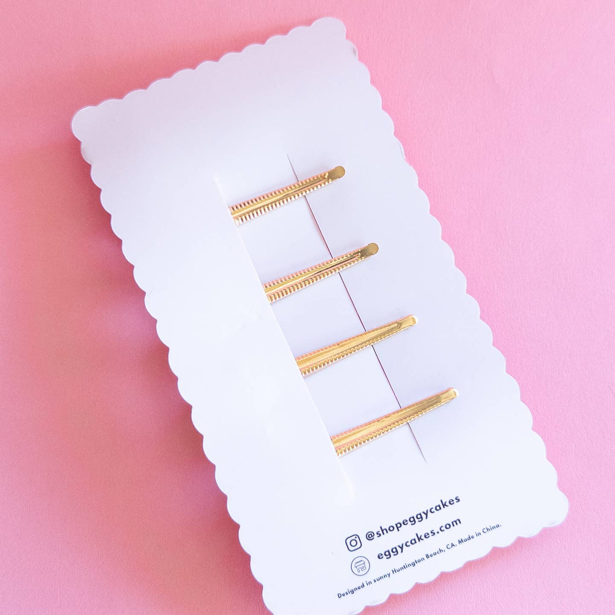 Set of gold hair clips on a white card with a pink background
