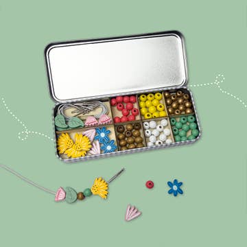 Metallic jewelry-making kit with beads and tools on a green background