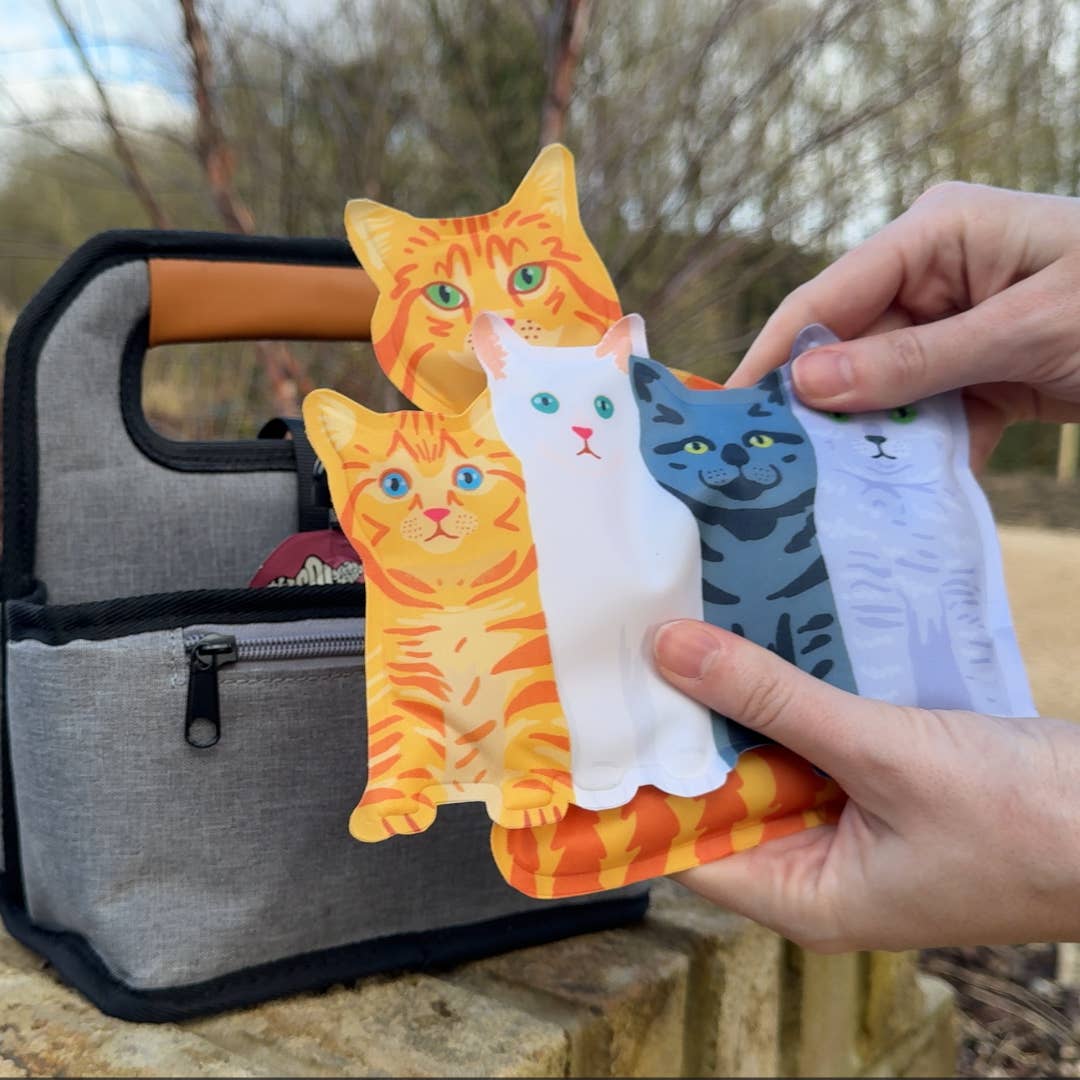 Four cat-shaped phone cases held by a hand with a gray bag in the background.