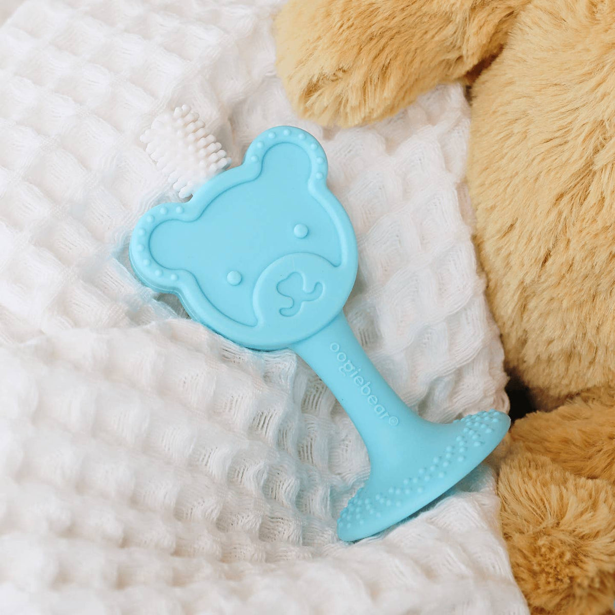 Blue teddy bear-shaped toy on a white blanket with a brown teddy bear in the background