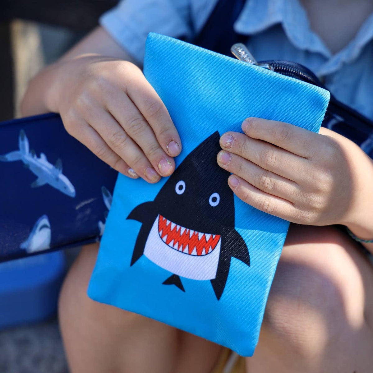 Child holding a blue pouch with a shark design