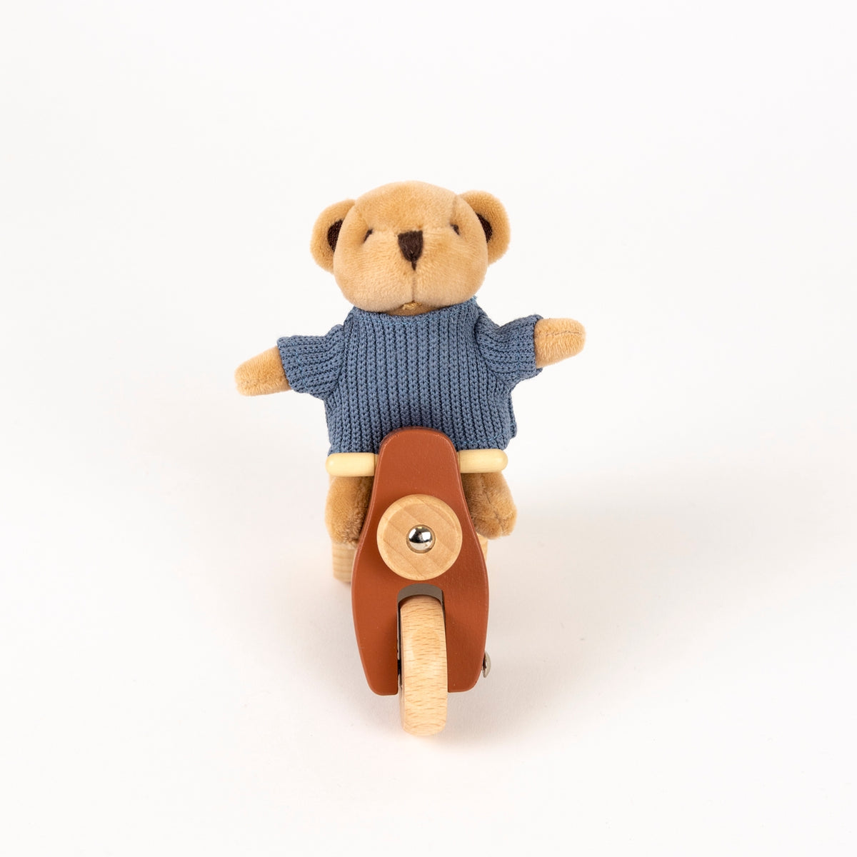 A small plush teddy bear wearing a blue knit sweater and riding a brown toy scooter, photographed against a clean white background.
