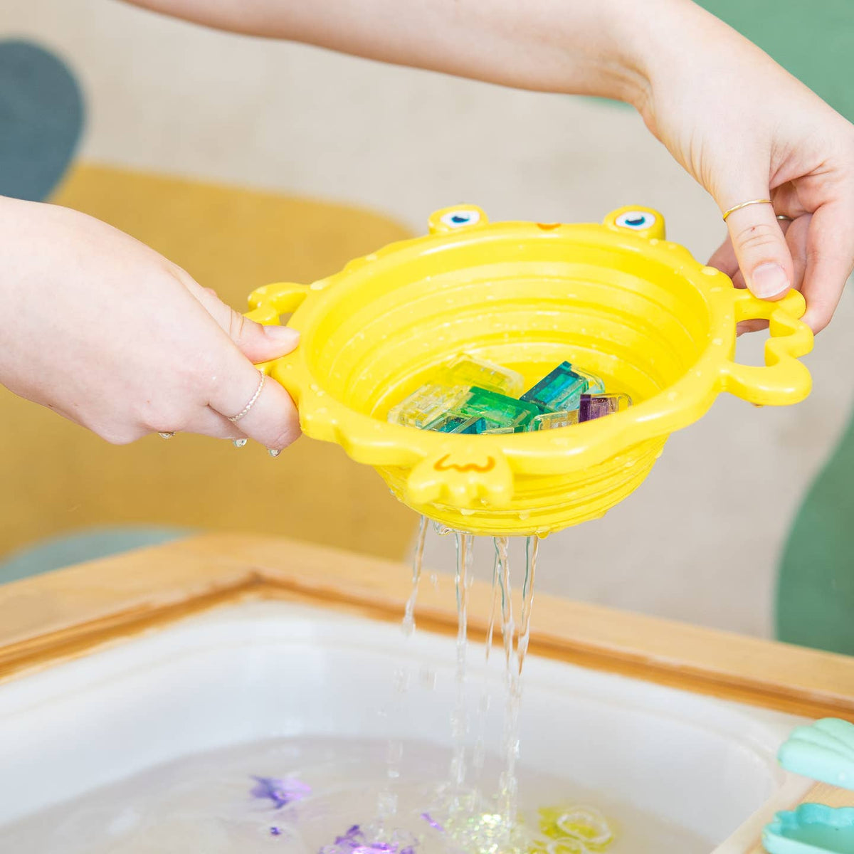 Yellow bath toy with water flowing out, held over a bathtub.