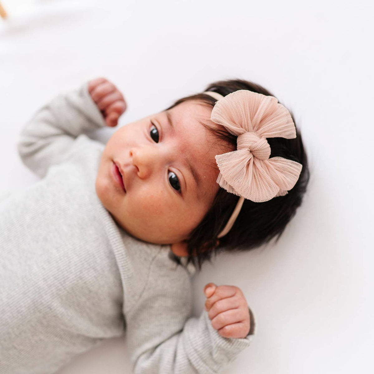 Baby wearing a light gray outfit and a large pink bow headband on a white background