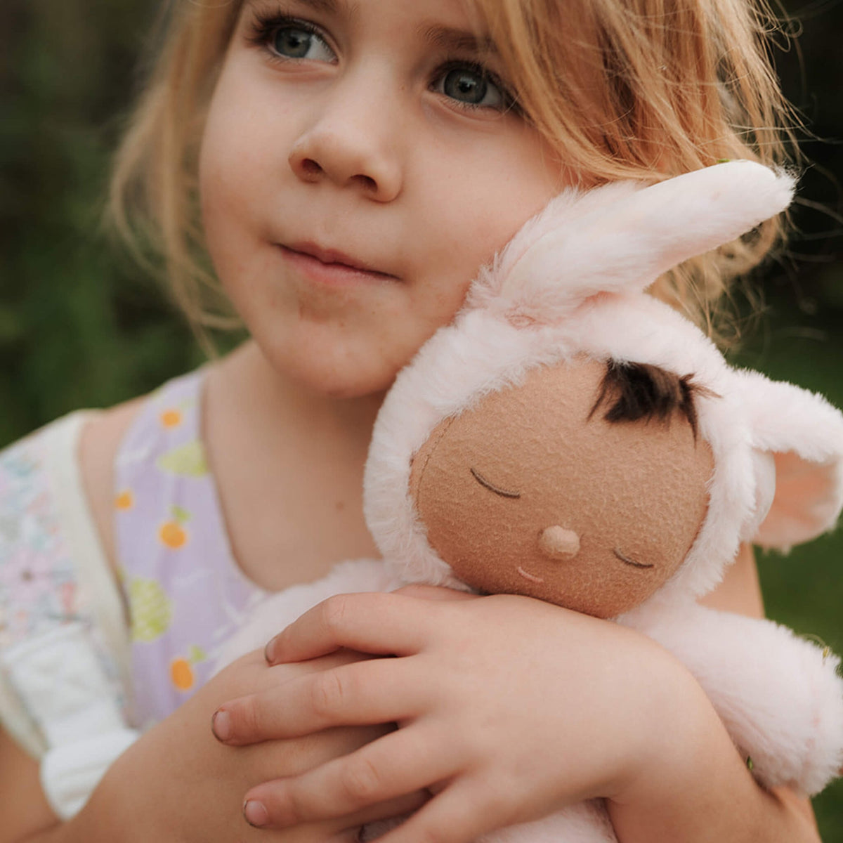 Young girl holding a plush toy with bunny ears outdoors