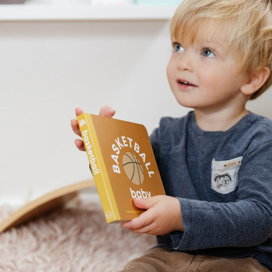 Child holding a book titled 'Basketball Baby' with a yellow cover.