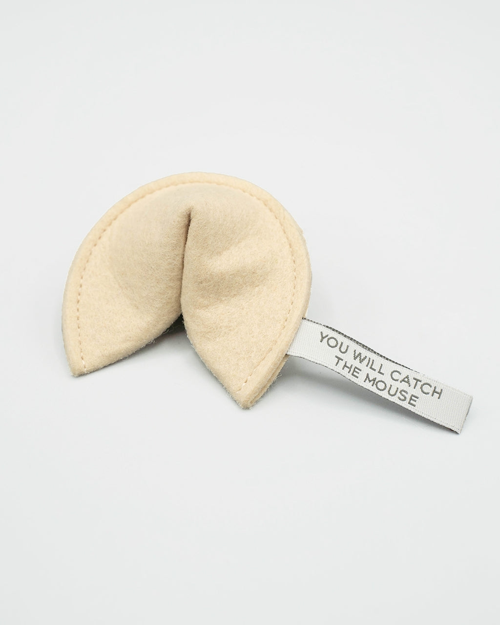 A cream-colored felt fortune cookie with a white paper tag attached that reads 'YOU WILL CATCH THE MOUSE' in black text, set against a plain light gray background.