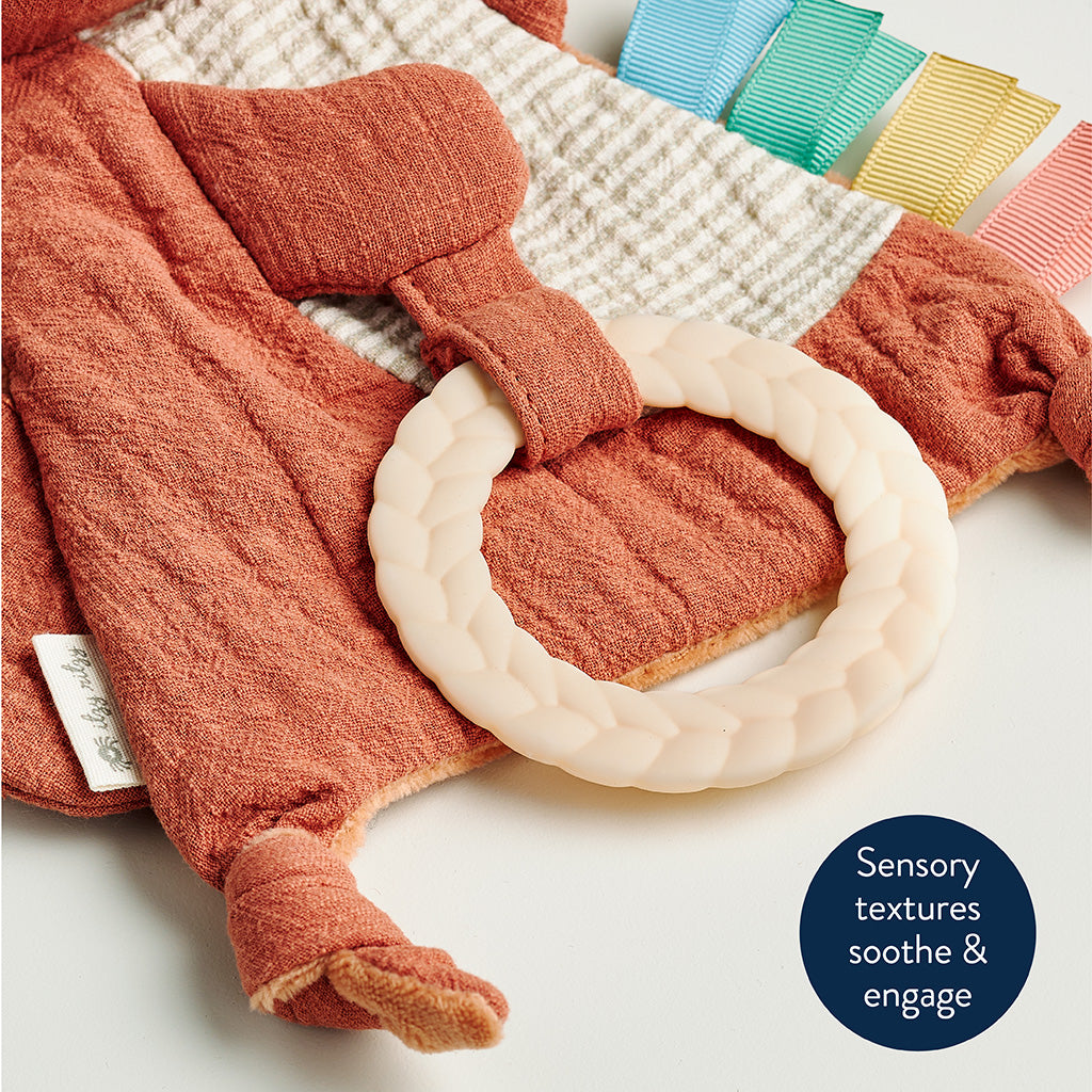 Textured orange baby blanket with a white ring and colorful clips on a neutral background.