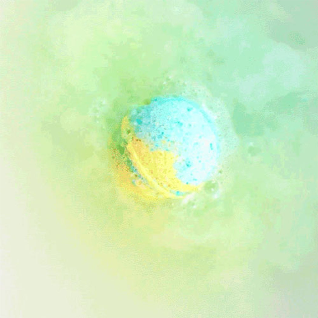 A round bath bomb or bath salt ball floating in soapy, pale green water with a blue and yellow color pattern.