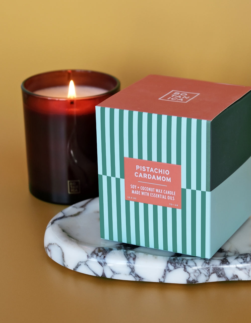 Candle and its packaging on a marble tray with a yellow background