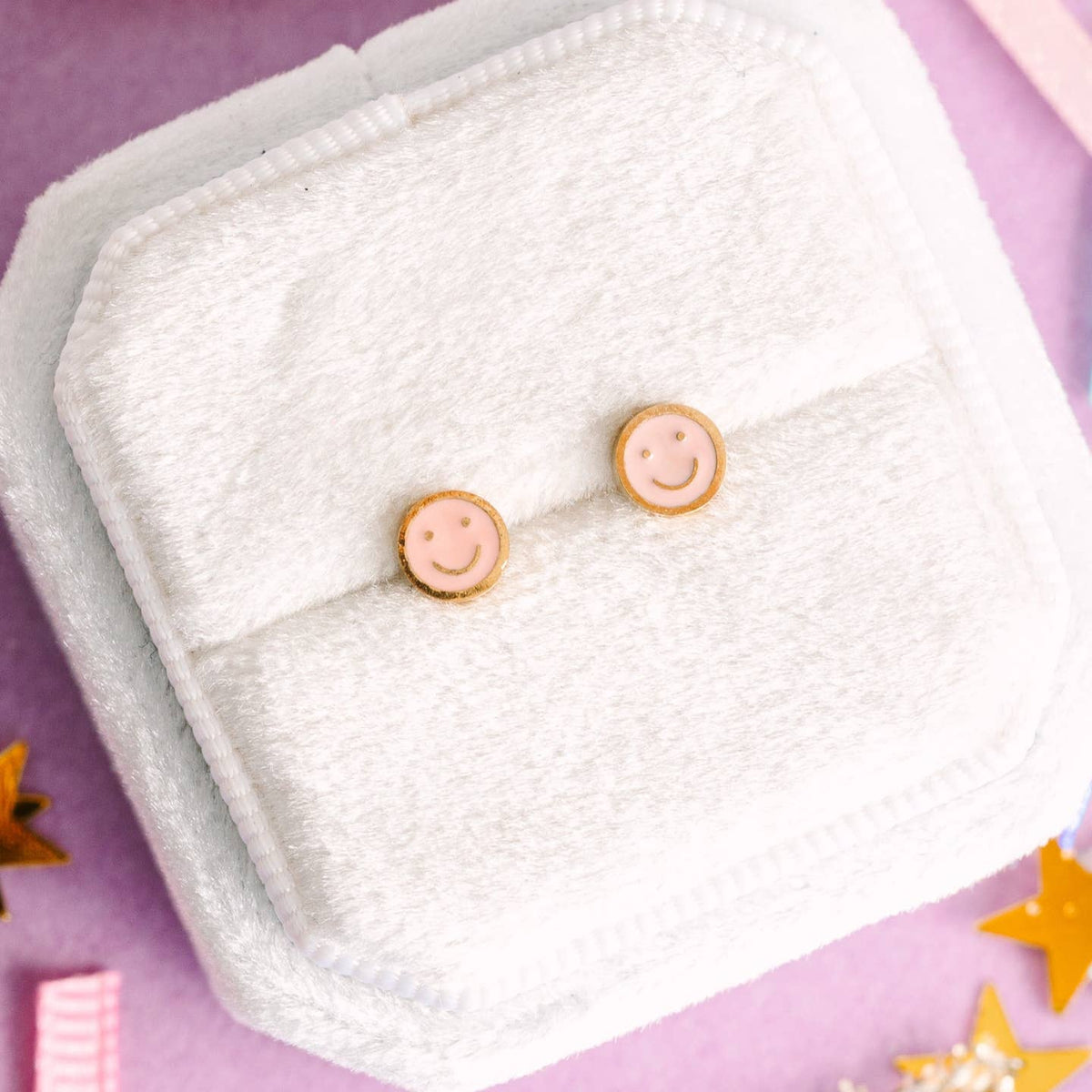 Smiley face earrings on a white cloth with a pink background