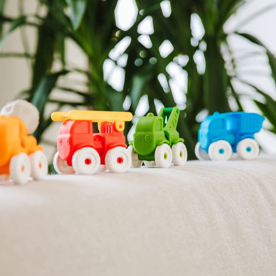 Colorful toy cars on a white surface with green plants in the background