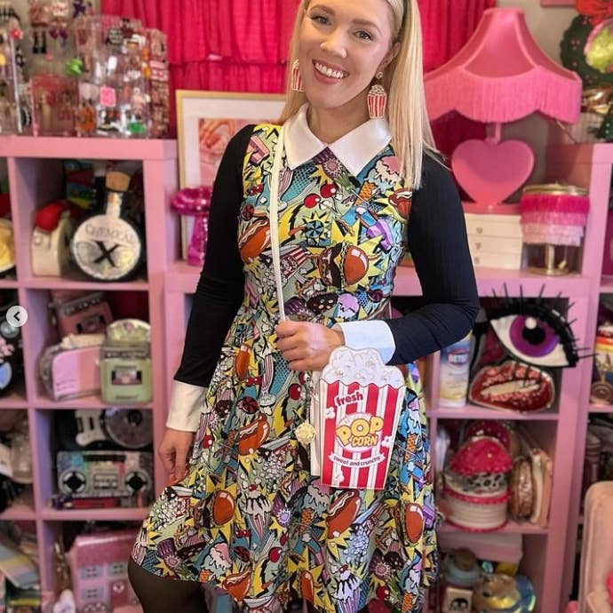 Woman in a colorful dress holding a popcorn box in a store with pink shelves and decorative items.