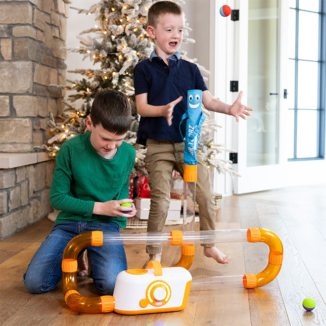 Two children playing with a toy laser pointer in a home setting with a Christmas tree in the background.