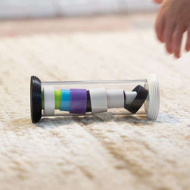 Colorful cylindrical toy on a carpet with a hand reaching towards it