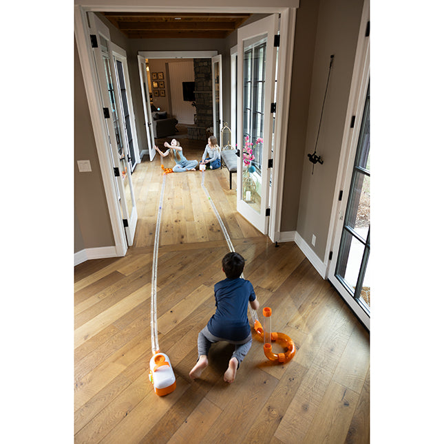 Child playing with toy vacuum cleaner on a wooden floor in a home setting.