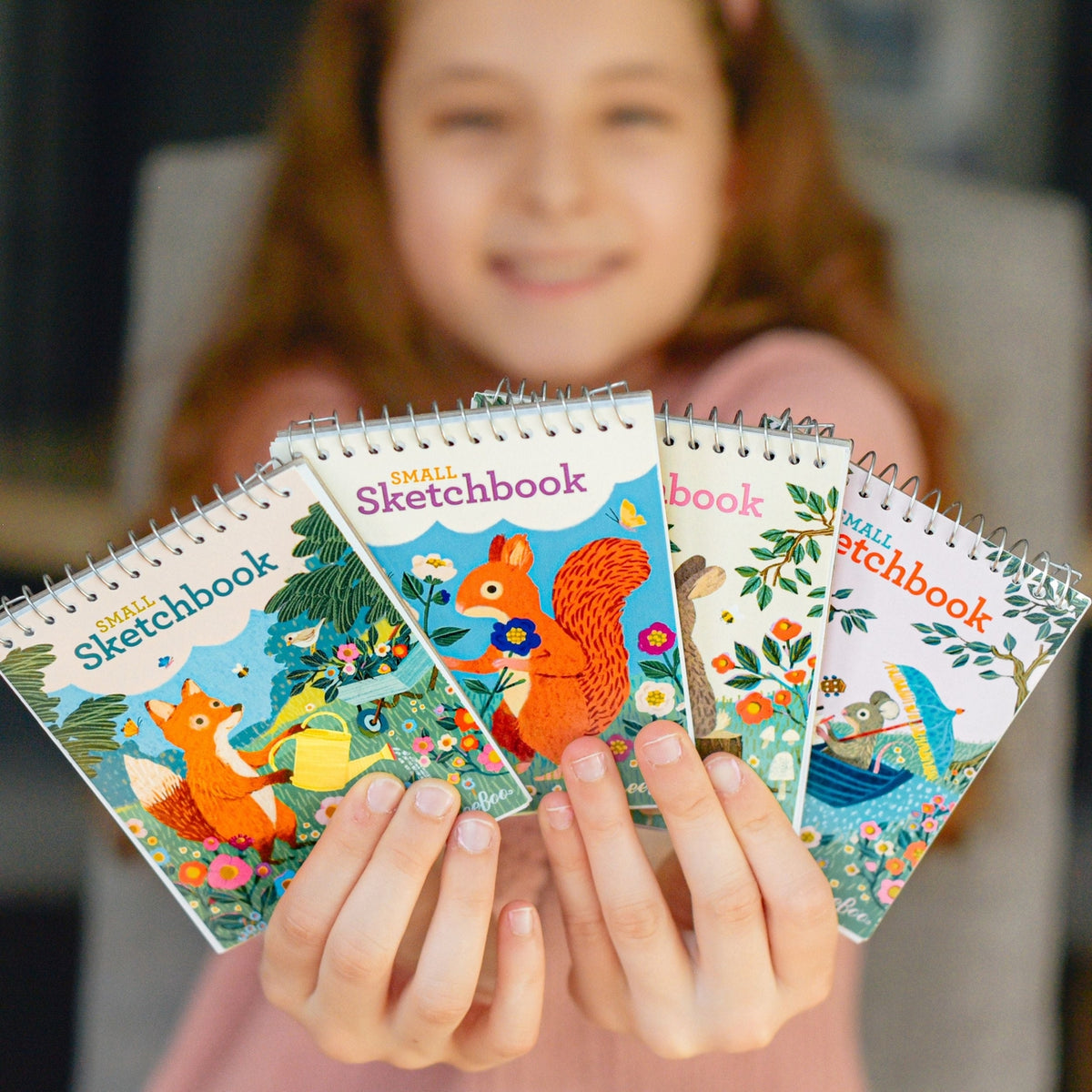 Child holding small sketchbooks with animal illustrations, blurred background