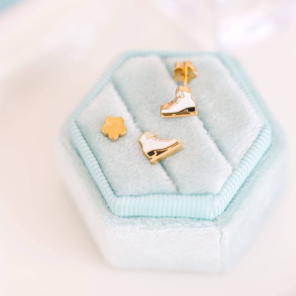 Gold ice skate earrings on a light blue hexagonal cushion