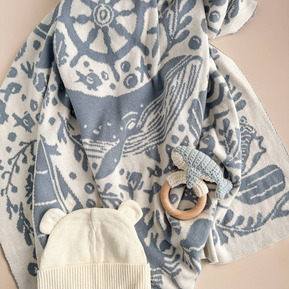 Baby hat and wooden ring toy on a blue and white patterned blanket