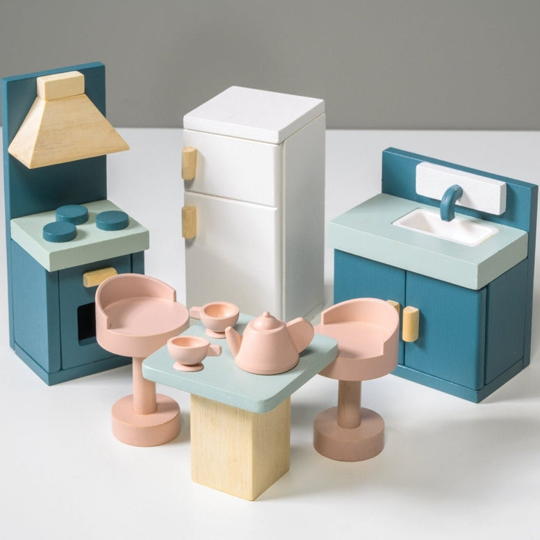 Wooden kitchen furniture set by Mentari against a white background, featuring a blue stove with an oven and hood, a white refrigerator with wooden handles, a blue sink unit with a cupboard, and a light wood-colored square table surrounded by four matching pinkish-tan stools.
