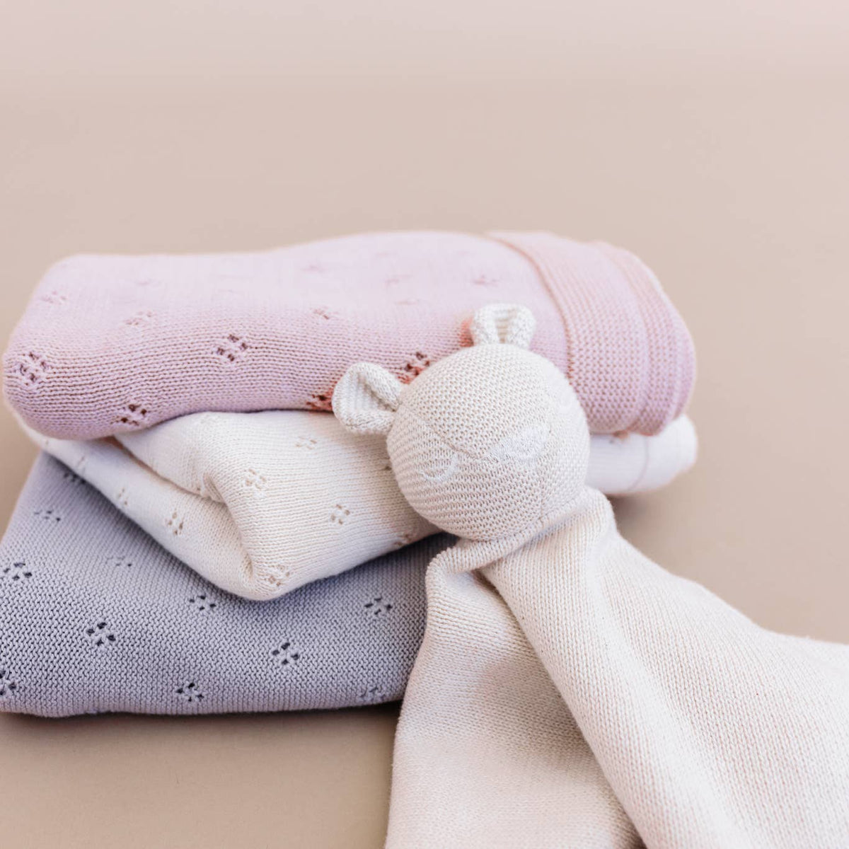 Stack of soft baby blankets with a toy on a beige background