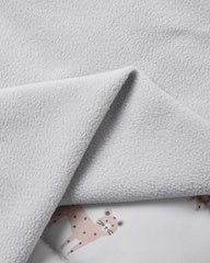 A close-up of a soft, light gray fleece blanket with a folded corner revealing a white underlay printed with a small pink spotted animal motif.