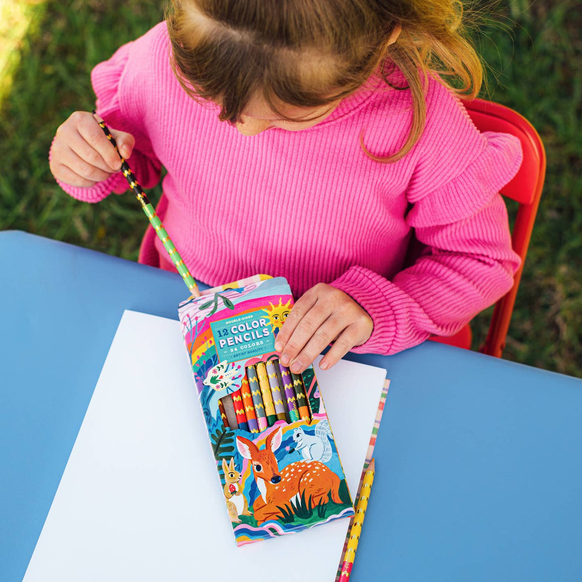 Child in pink sweater holding a set of colored pencils outdoors
