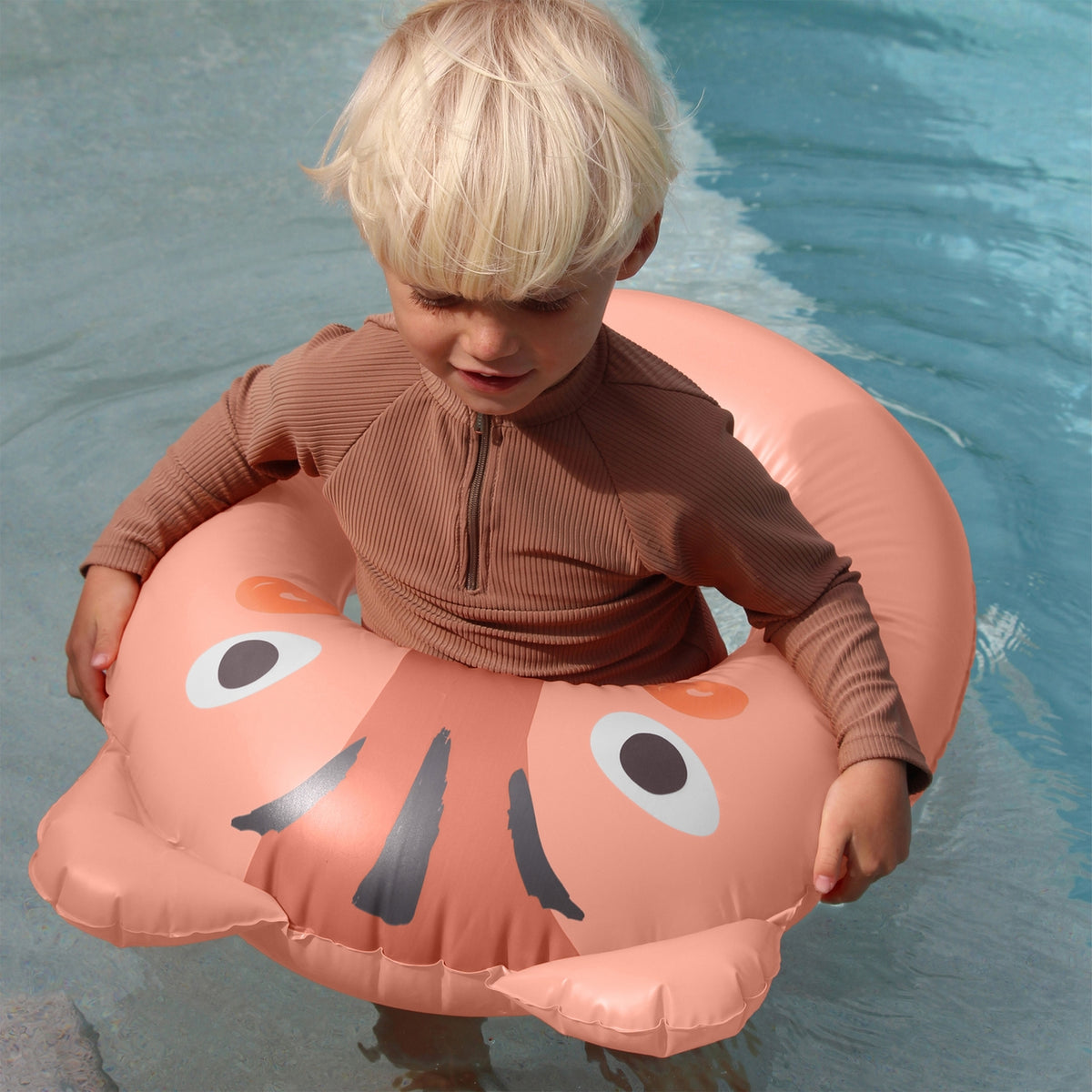 Child in a pool with a pink inflatable ring featuring a face design