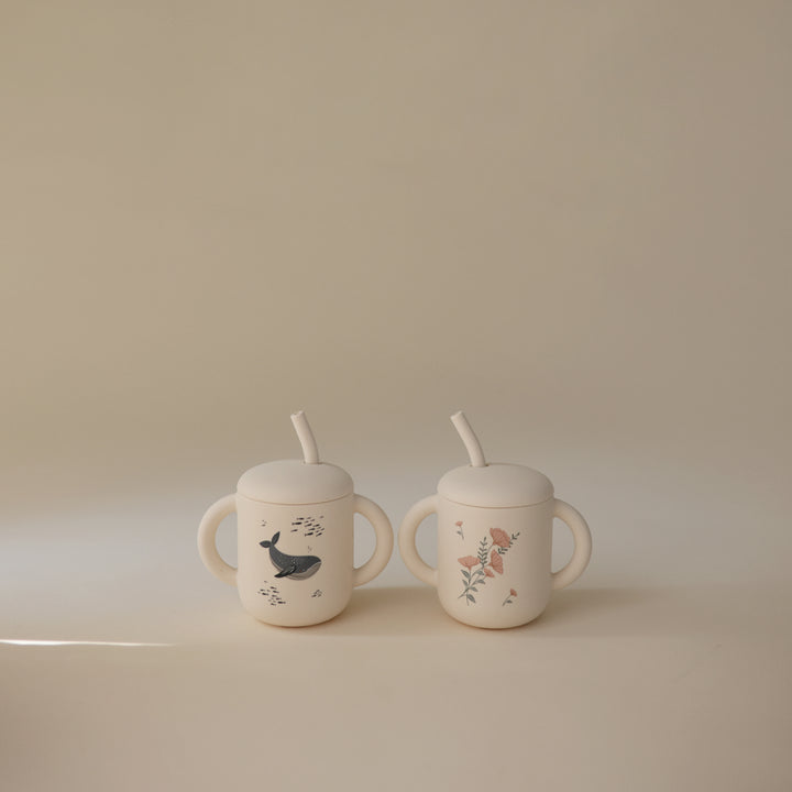 Two ceramic sippy cups with animal illustrations on a beige background