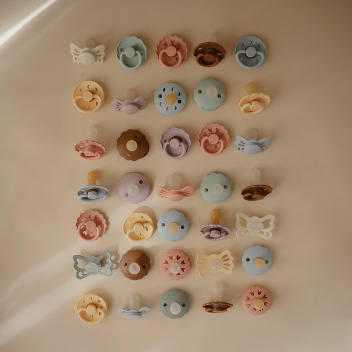 Collection of colorful pacifiers arranged in a grid on a beige surface