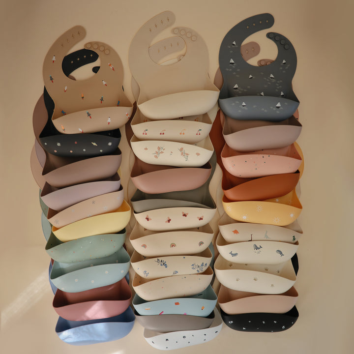 Stack of colorful baby bibs with various patterns on a beige background