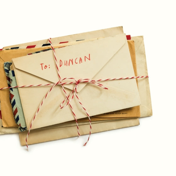 A stack of vintage-style envelopes tied with red-and-white bakers twine, with the top envelope addressed 'To: DUNCAN' in red handwriting, photographed on a clean white background.