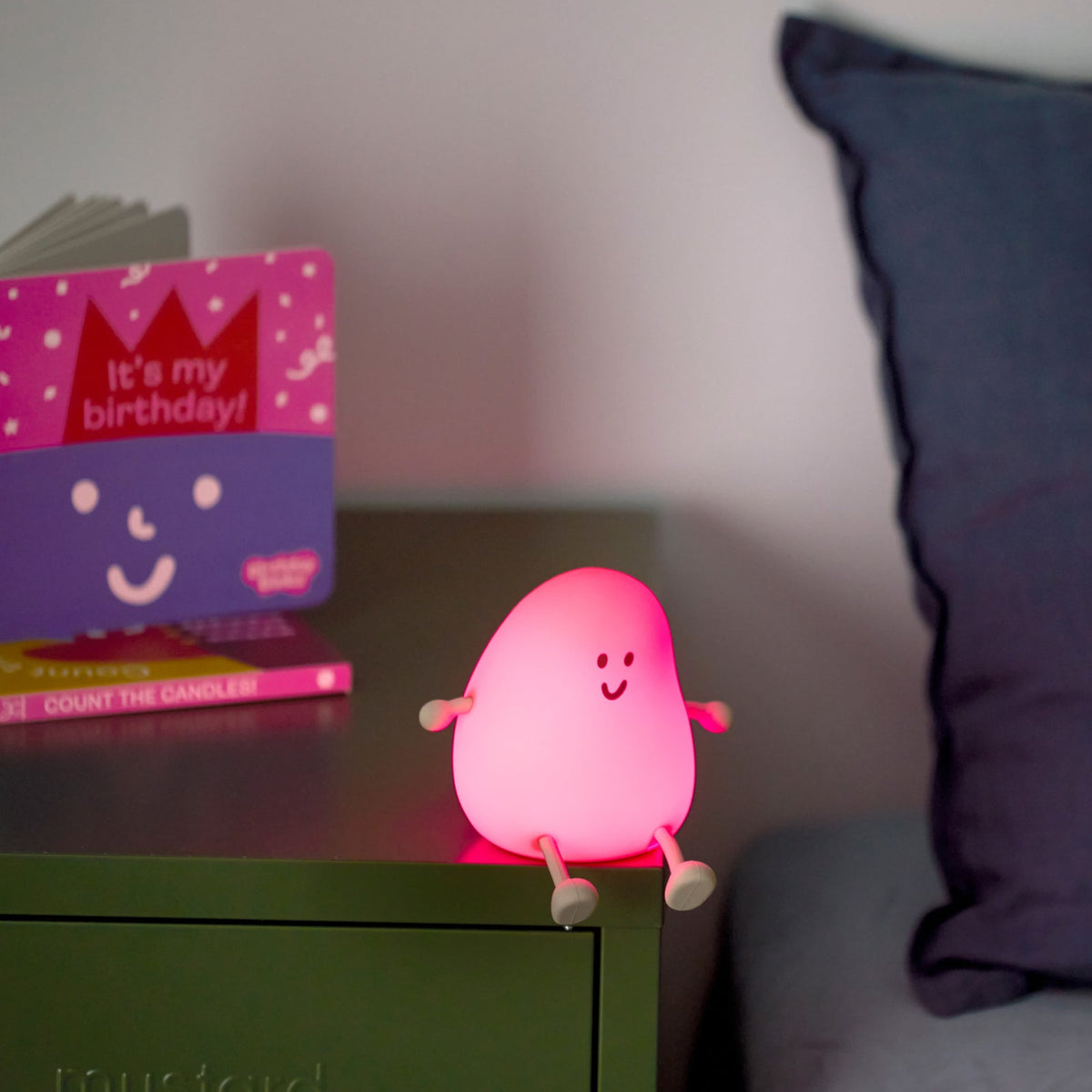 Pink character light on a nightstand with a purple pillow and birthday card in the background