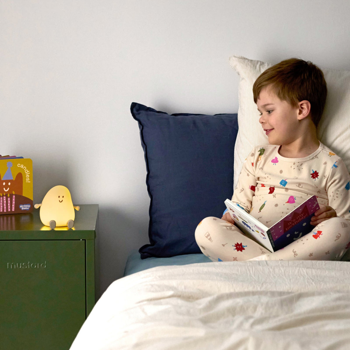 Child reading a book in bed with a nightlight and colorful pillow