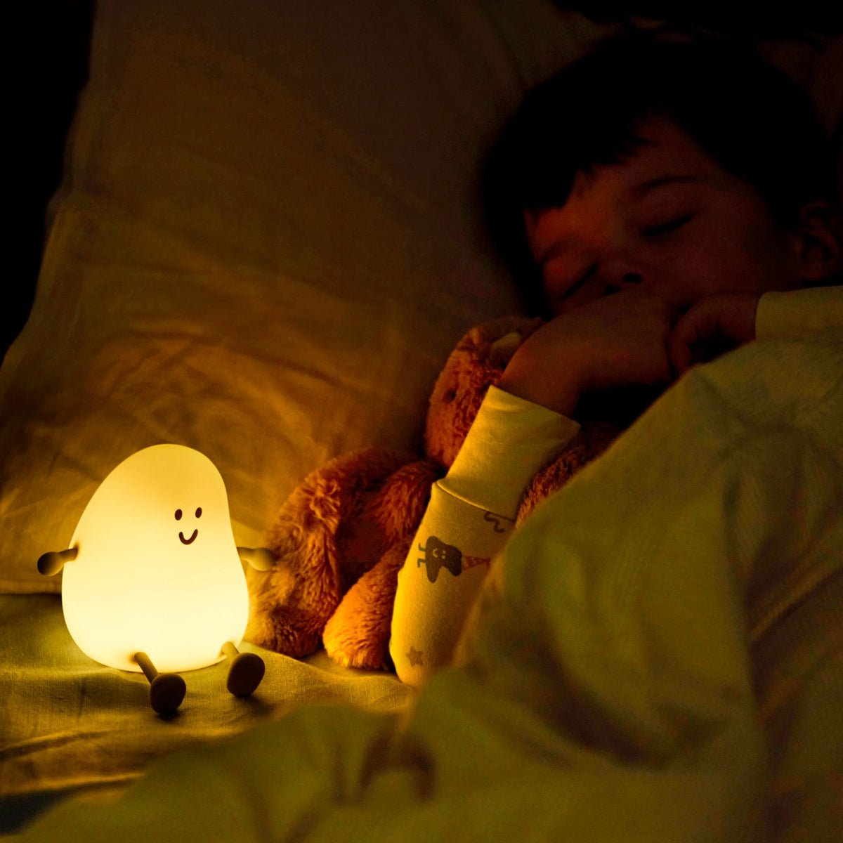 Child sleeping with a plush toy and a glowing night light in a dark room