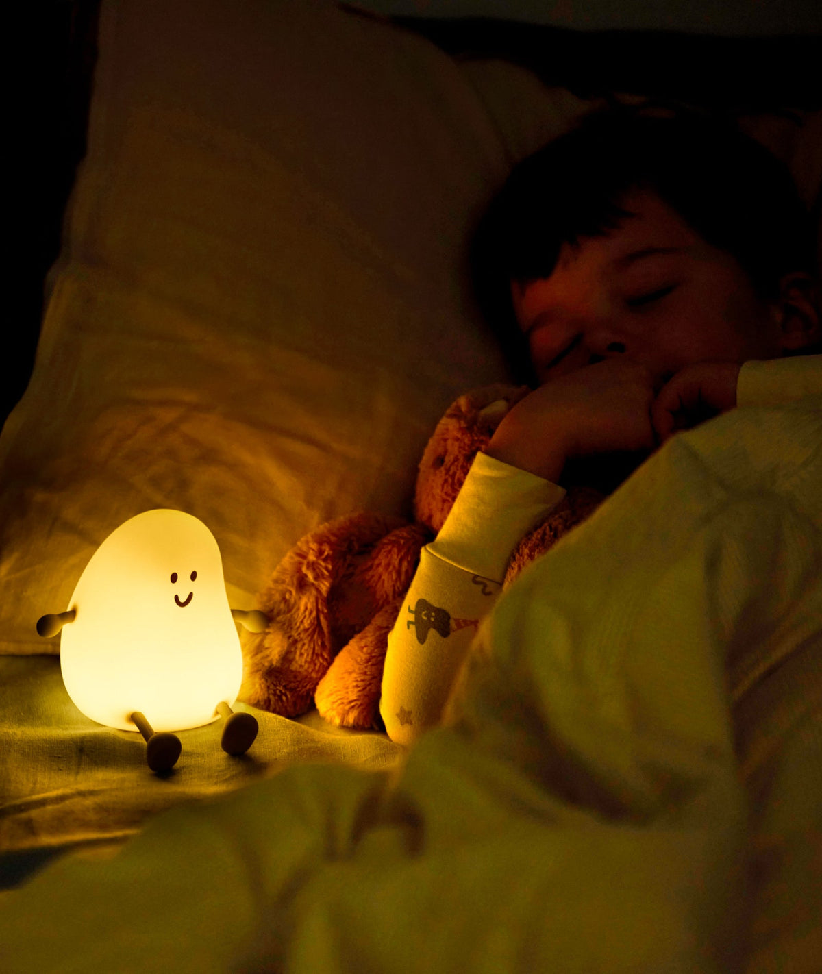 Child sleeping with a plush toy and a glowing night light in a dark room
